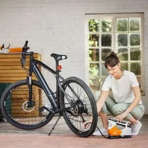 a woman using the STIHL KOA 20 Cordless Compressor to pump up a bicycle tyre indoors