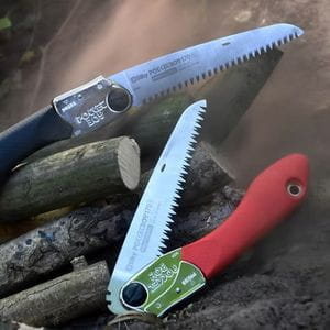 a straight Silky Pocketboy saw with a black handle and a partially closed Silky Pocketboy saw with a red handle, both resting on a pile of cut branches
