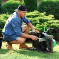 a young man wearing a baseball cap back-to-front, brushing down the underside of a lawnmower