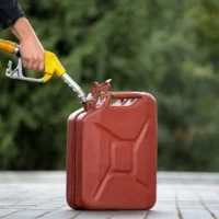 someone filling a red fuel can, which is sat on a patio, using a yellow fuel nozzle