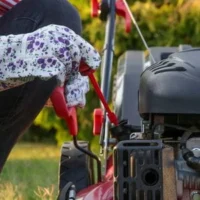 a woman wearing flower-patterned gloves, checking a lawnmower's oil level using a dipstick