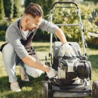 a young man wearing protective glasses, attempting to fix a lawnmower