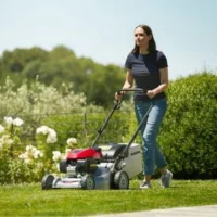 a woman mowing a lawn using the Honda HRG466 mower, with trees and shrubs in the background