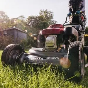 a close up of the Honda HRH 536 HX Mower cutting a lawn, with trees and a house in the background