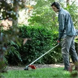 a young man wearing ear defenders, using a Husqvarna grass trimmer to cut the edge of a lawn
