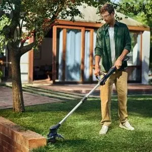 a man cutting the edge of a lawn, next to a garden wall, using a Husqvarna grass trimmer
