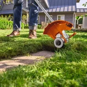 a close up of someone using the STIHL FSA 50 Cordless Grass Trimmer to tidy lawn edges around a stone strip