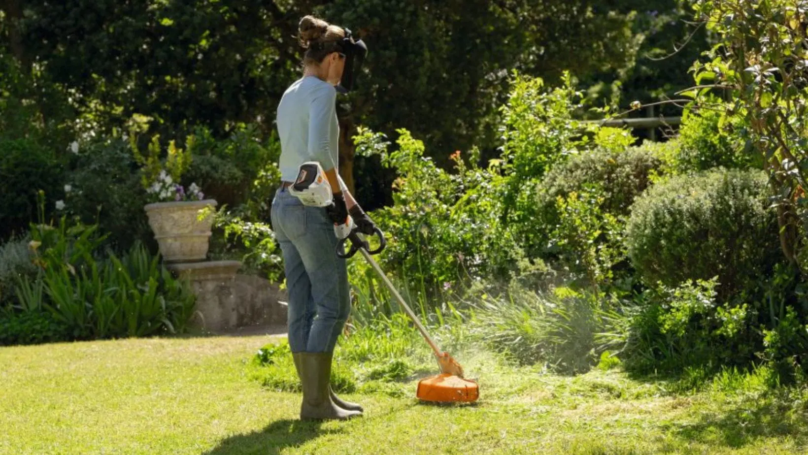 STIHL FSA 60 Cordless Grass Trimmer (1) a rear view shot of a woman using the STIHL FSA 60 Cordless Grass Trimmer in a garden