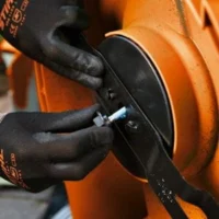 a close up of someone wearing black, STIHL-branded gloves, removing the blade from an orange lawnmower