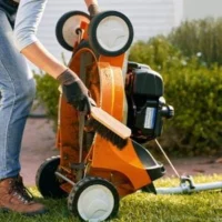 a woman brushing down the underside of an orange STIHL lawnmower