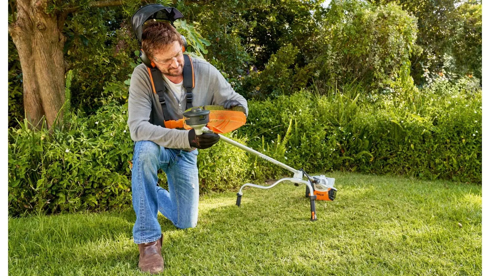 a man knelt down on a lawn, checking the strimmer line on a STIHL grass trimmer