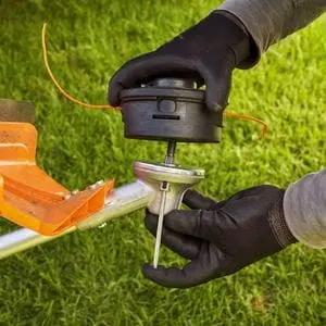 someone wearing black gloves, removing the strimmer head from a grass trimmer