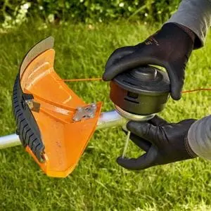 someone wearing black gloves, removing the strimmer head from a STIHL grass trimmer