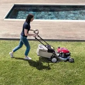 a woman using a Honda IZY HRG 466 SKEP Petrol Lawn Mower near to a swimming pool
