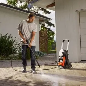 a man cleaning a driveway using the Husqvarna PW 240 Electric Pressure Washer