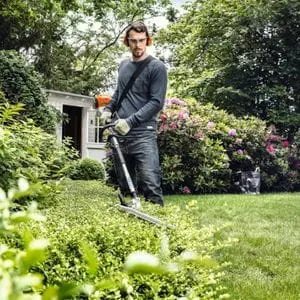 a man in a garden, using the STIHL HL-KM 145° Long-Reach Hedge Trimmer KombiTool to cut a low-lying shrub