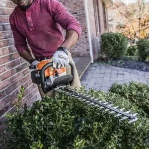 a man using the STIHL HS 45 Petrol Hedge Trimmer to shape a shrub outside a red brick property