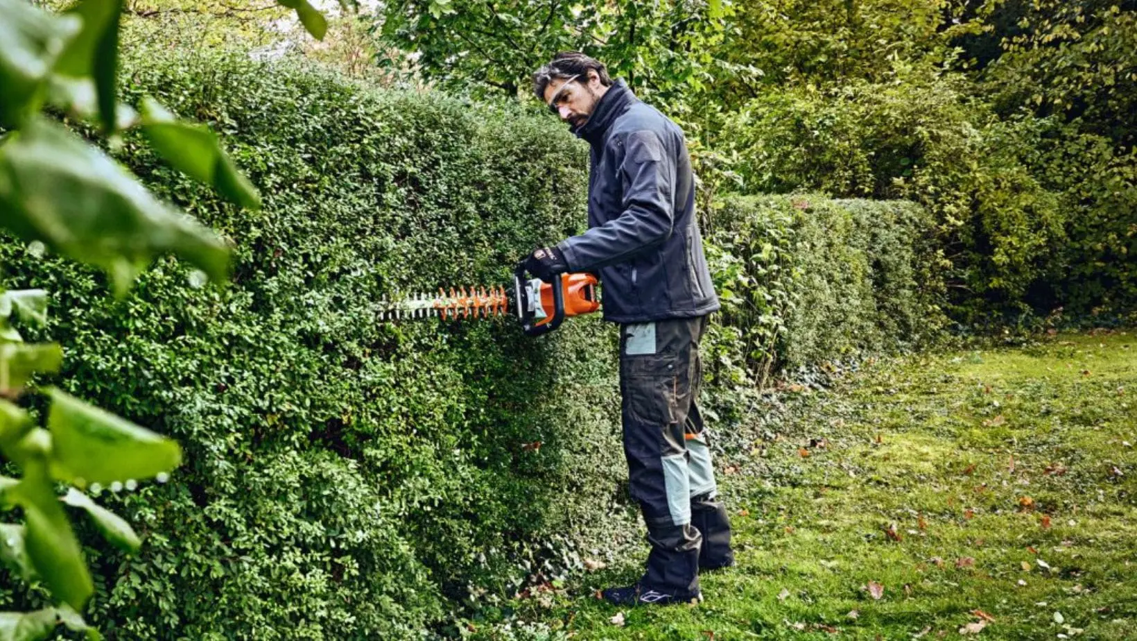 STIHL HSA 100 Cordless Hedge Trimmer (1) a man carefully cutting the side of a long garden hedge using the STIHL HSA 100 Cordless Hedge Trimmer