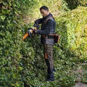 a man dressed in protective glasses and STIHL-branded clothing, using the STIHL HSA 130 Cordless Hedge Trimmer to trim a large hedge