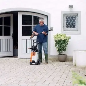 a man with grey hair, outside a large white house, adjusting the spray lance on a STIHL pressure washer