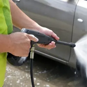 somebody adjusting a pressure washer near a car