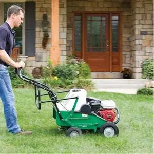 a man pushing the Billy Goat AE401H Petrol Lawn Aerator across a lawn, at the front of a house