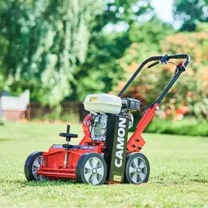 the Camon LS42-B1 Lawn Scarifier sat on a lawn, with trees, shrubs, and the corner of a building in the background