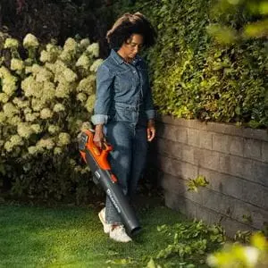 a woman using a Husqvarna leaf blower to move hedge clippings from a lawn