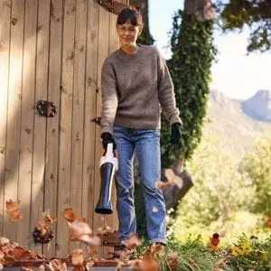 a woman using the STIHL BGA 30 Cordless Handheld Leaf Blower to move leaves away from garden fencing