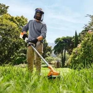 a front-facing shot of a man using the STIHL FSA 70 Cordless Brushcutter to cut long grass in a large garden