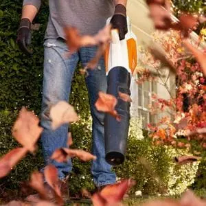 someone wearing gloves, tidying leaves in a garden using a STIHL leaf blower