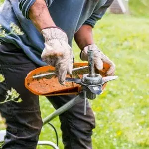 a close-up of a man wearing gloves, removing the blade from a STIHL brushcutter