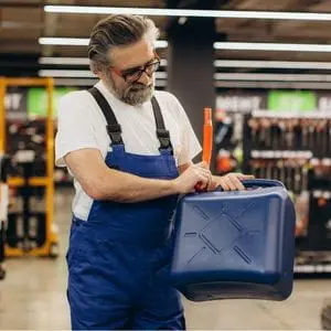 a man wearing blue dungarees, fitting a funnel to a jerrycan