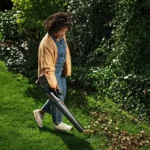 a woman using the Husqvarna Aspire™ B8X-P4A Cordless Handheld Leaf Blower to clear leaves from a lawn