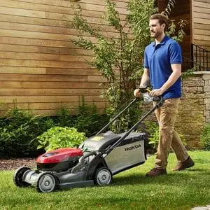 a man wearing a blue polo shirt and beige trousers, mowing a lawn near a house