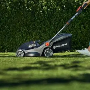 someone cutting a lawn in front of a hedge, using the Husqvarna Aspire™ LC34-P4A Lawnmower