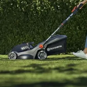 someone mowing a lawn next to a hedge with a Husqvarna Aspire™ LC34-P4A Cordless Lawn Mower