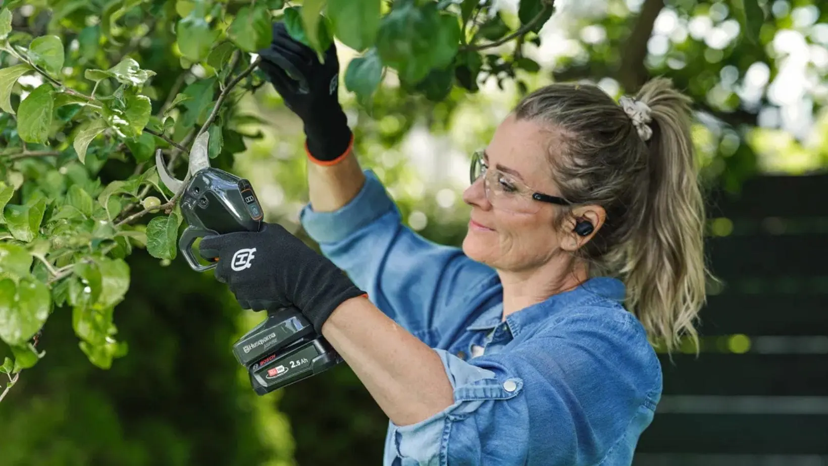 PS30X-P4A Secateurs (1) a woman with a pony tail and wearing safety glasses, using the Husqvarna Aspire™ PS30X-P4A Secateurs to prune a tree