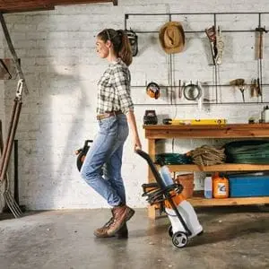 a woman wheeling a STIHL RE 80 Electric Pressure Washer out of a white-walled garage