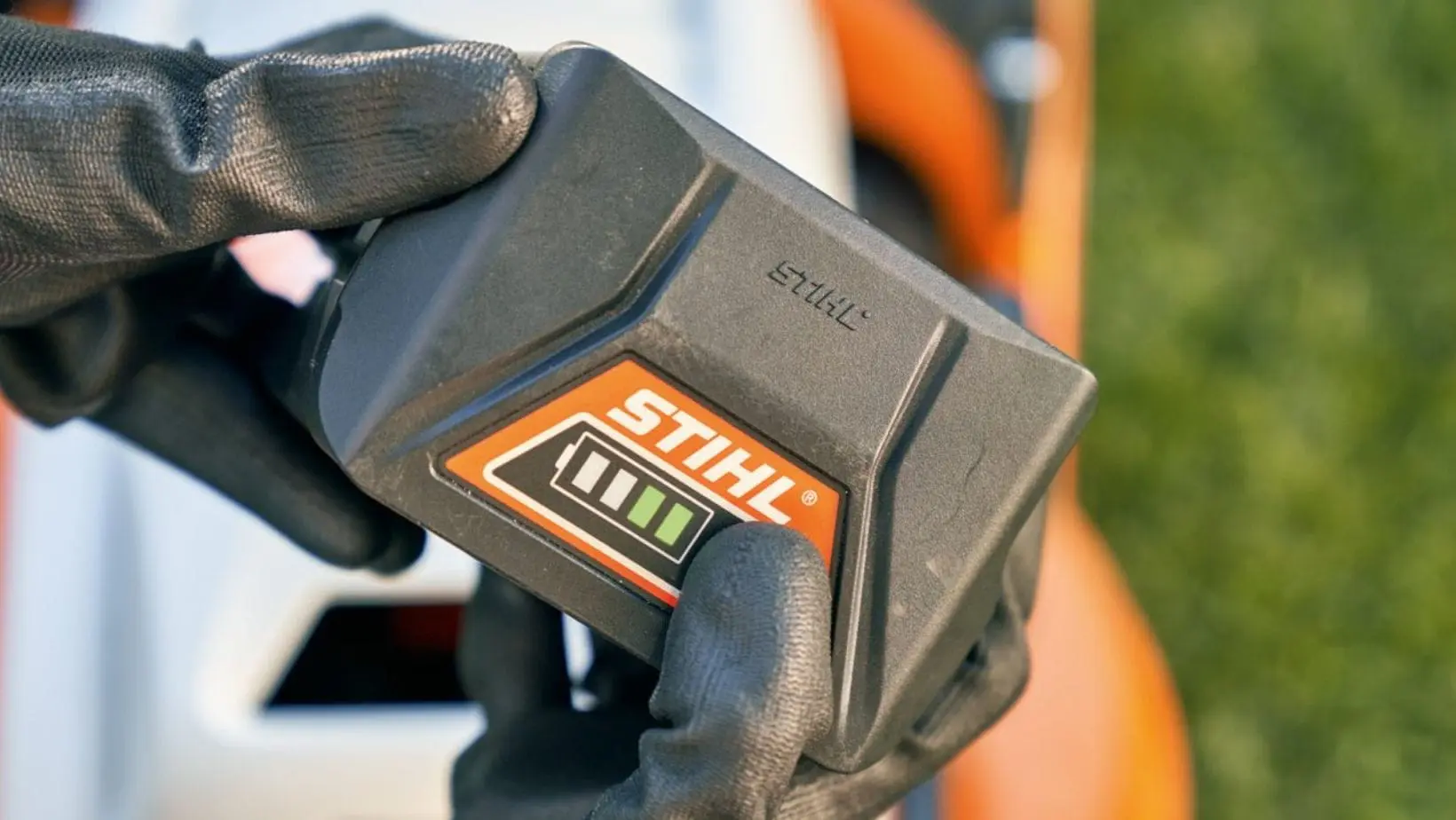 STIHL battery main (1) someone wearing gloves, holding a STIHL battery