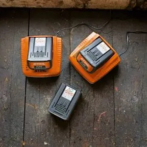 3 STIHL batteries, 2 of which are in STIHL chargers, all on a wooden table