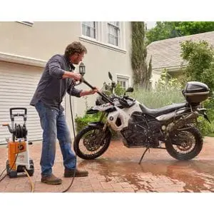 a man using a STIHL power washer to clean a motorbike on a driveway