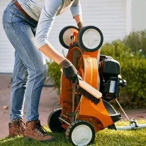 a woman brushing down the underside of an orange STIHL lawnmower