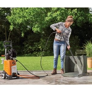 a woman using a STIHL pressure cleaner to wash a grey rattan chair on a patio