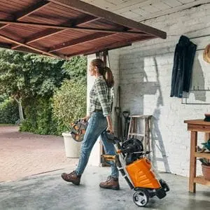 a woman wheeling a STIHL pressure washer out of a white-walled garage