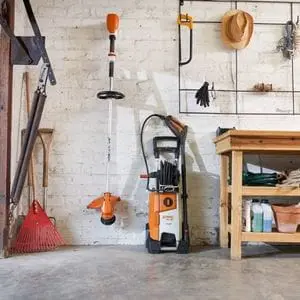 a brushcutter, pressure washer, plus other tools and accessories, neatly stored in a white-walled garage