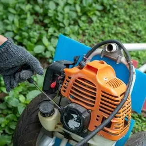 a gloved hand pulling a petrol lawn mower starter cord