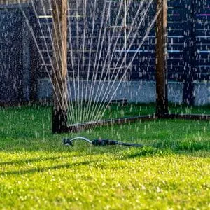 water coming out of a sprinkler on a lawn, with a wooden structure and slatted fence panels in the background