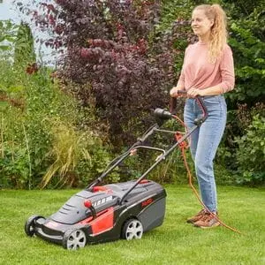 a woman holding the handle of the AL-KO 34.4 E COMFORT Electric Lawn Mower, which is parked on a lawn