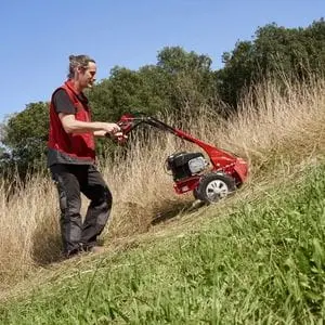 a man using the AL-KO BM 5001-R IV Petrol Scythe Mower to cut long grass on a steep hill
